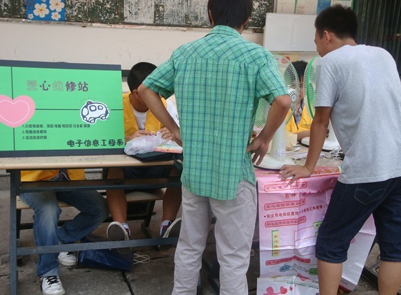 图为：大二同学请爱心维修站队员维修电风扇